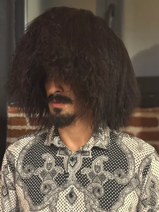 Black sheepskin papakha with long wavy wool, worn by a man, front view, head slightly turned