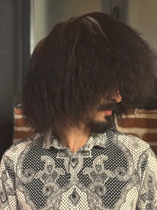 Black sheepskin papakha with long wavy wool, worn by a man, three-quarter view