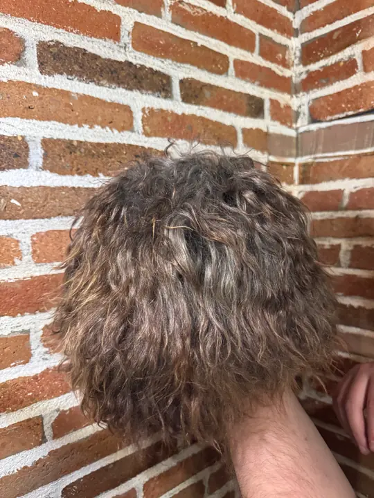 Goat fur papakha held in a hand against a brick wall, showing the curly fur