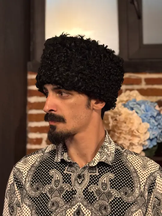 Black karakul papakha with short tight curls, worn by a man, side view facing left