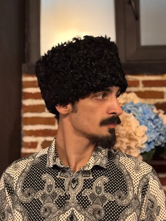 Black karakul papakha with short tight curls, worn by a man, side view facing right
