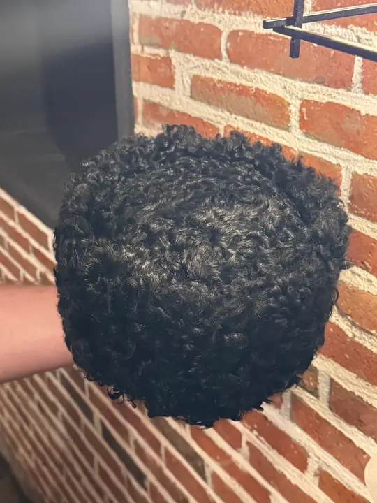 Black karakul papakha held in a hand against a brick wall, seen from above