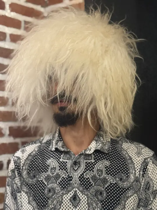 White sheepskin papakha with long wool falling over the face, worn by a man, front view