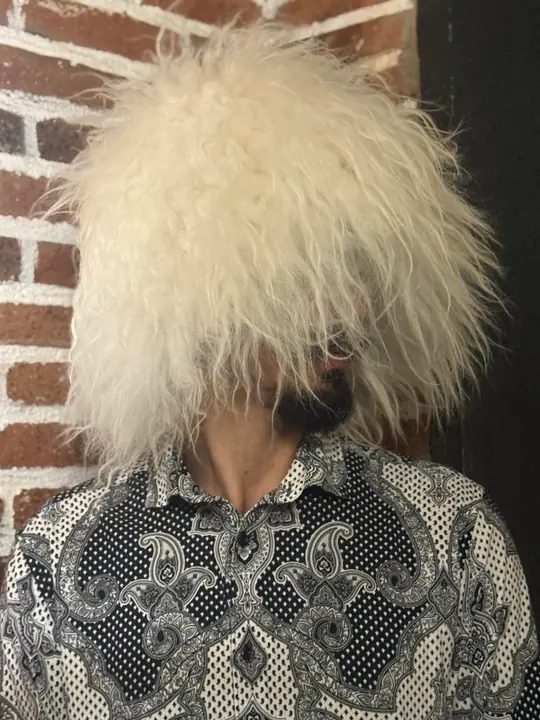 White sheepskin papakha with long straight wool, worn by a man, front view, head slightly turned