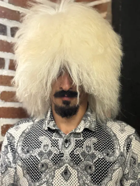White sheepskin papakha with long straight wool, worn by a man looking at the camera, front view