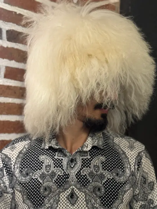 White sheepskin papakha with long straight wool, worn by a man looking down, three-quarter view
