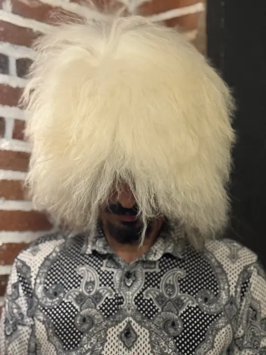 White sheepskin papakha with long straight wool, worn by a man, front view from slightly above