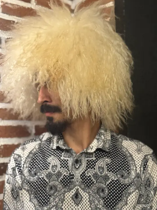 White sheepskin papakha with long wavy wool, worn by a man, side view