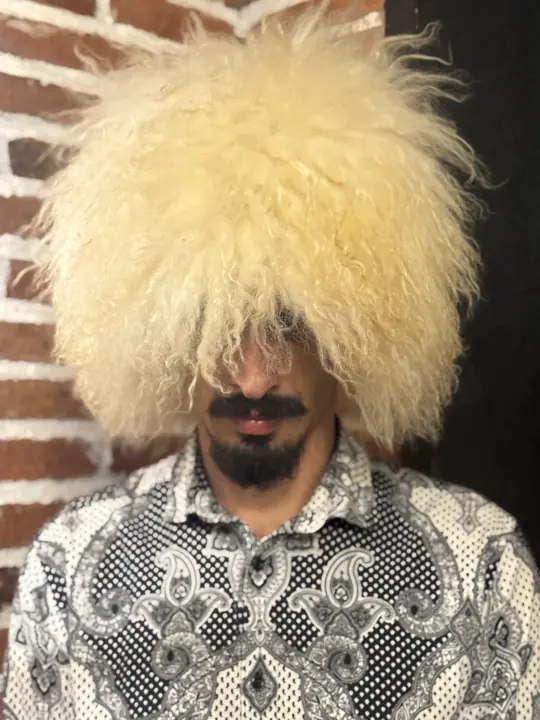 White sheepskin papakha with long wavy wool, worn by a man, front view, head slightly turned