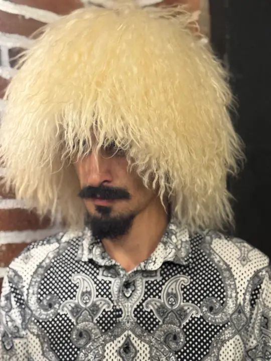 White sheepskin papakha with long wavy wool, worn by a man, three-quarter view