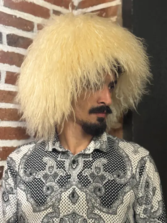 White sheepskin papakha with long wavy wool, worn by a man, side view, looking down