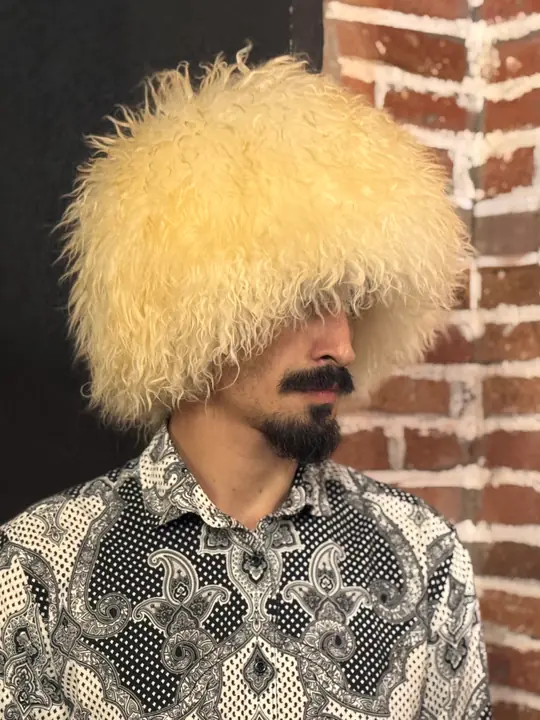 White sheepskin papakha with long wavy wool, worn by a man, side view